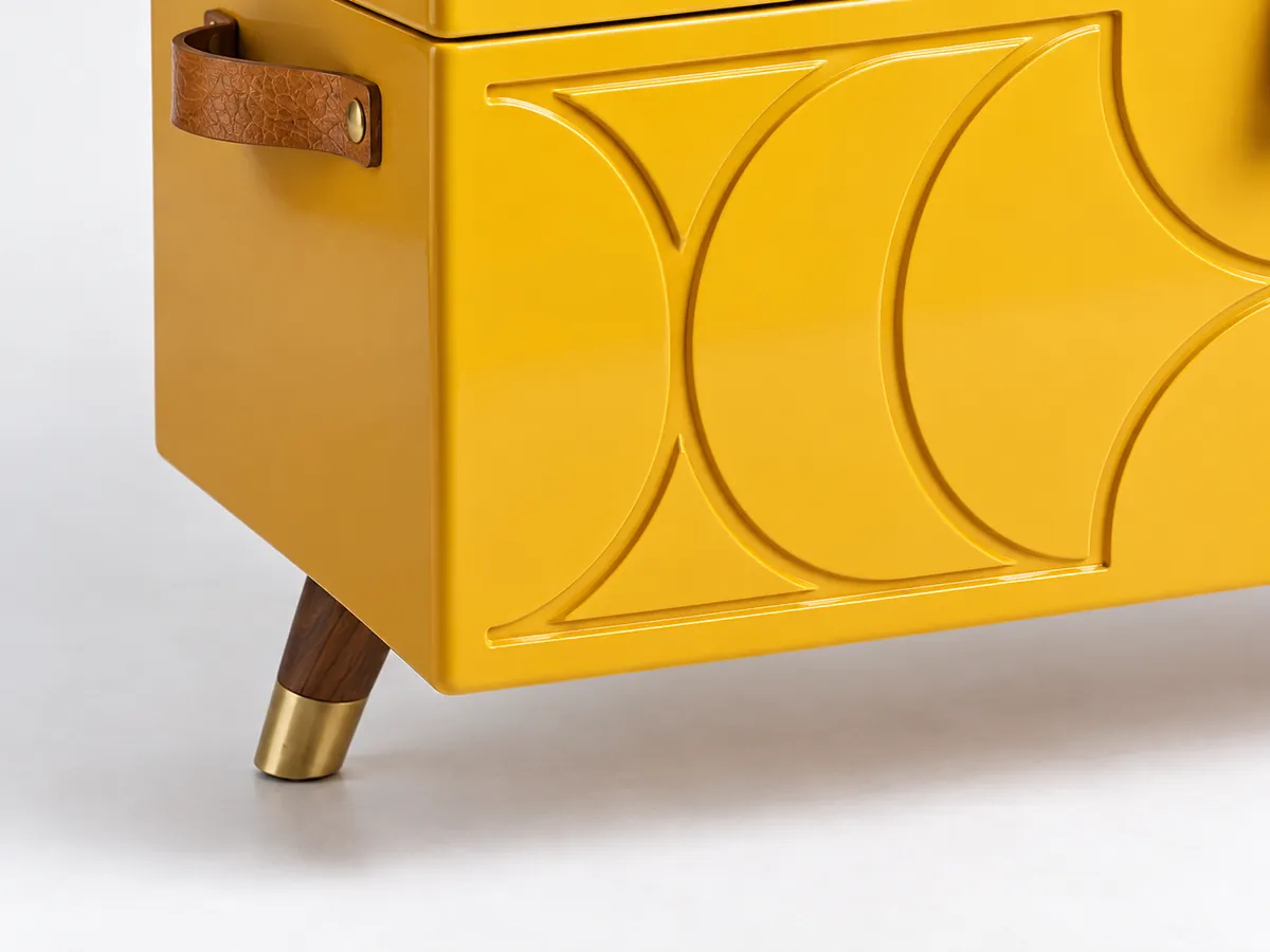 Close-up of routed arches on a glossy yellow painted chest and a dark splayed leg with a brass tip — AI concept