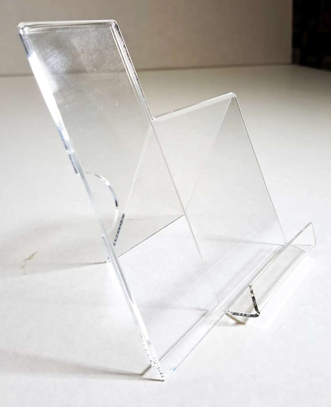 Clear acrylic stand with a slanted back and a front lip, for a card or a phone