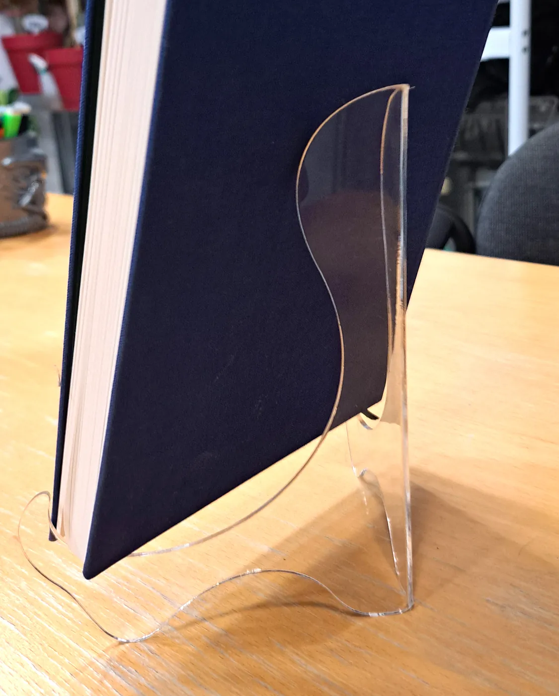 Clear curved acrylic stand holding a dark blue book upright on a table