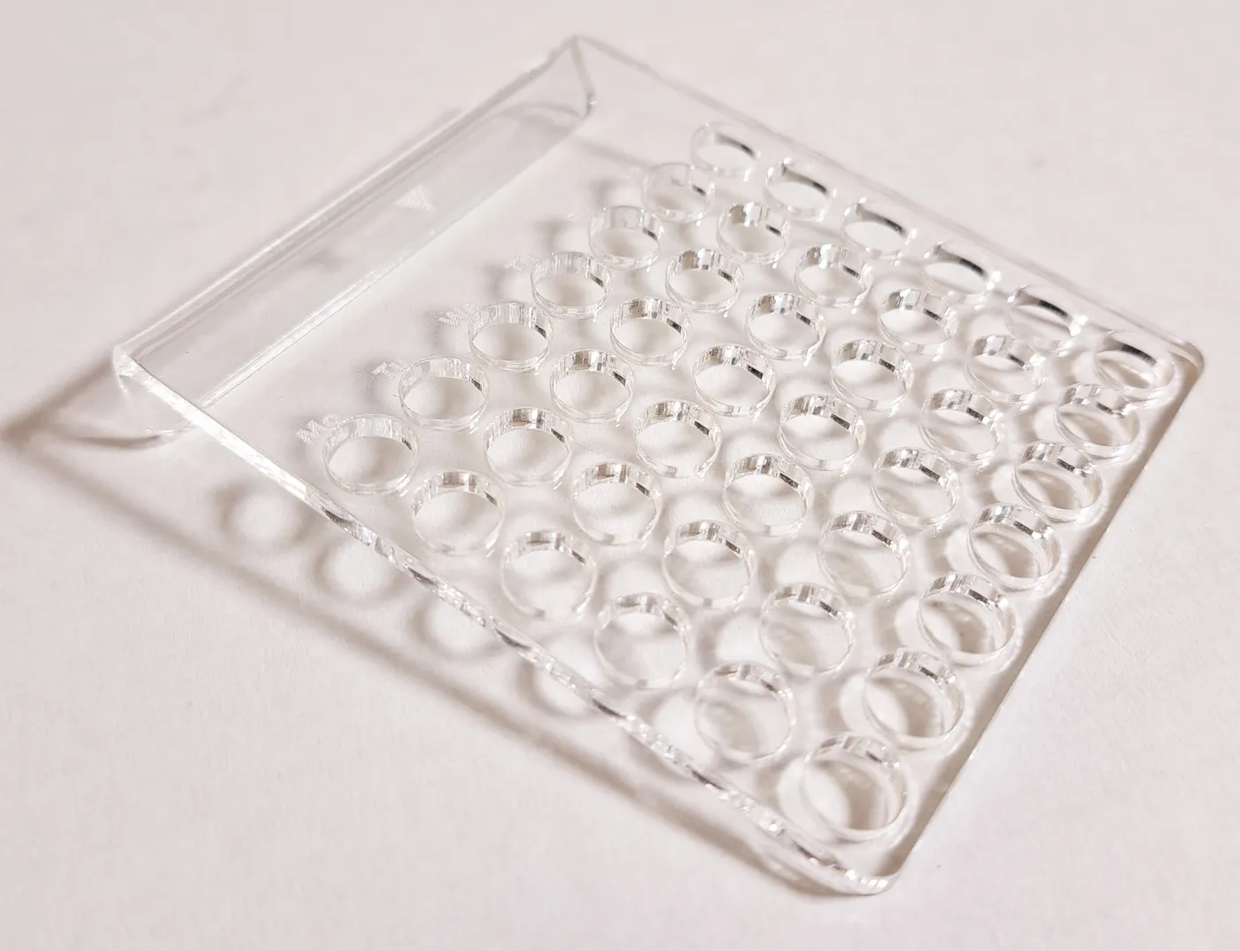 Clear acrylic tray with a grid of round holes and a raised back edge