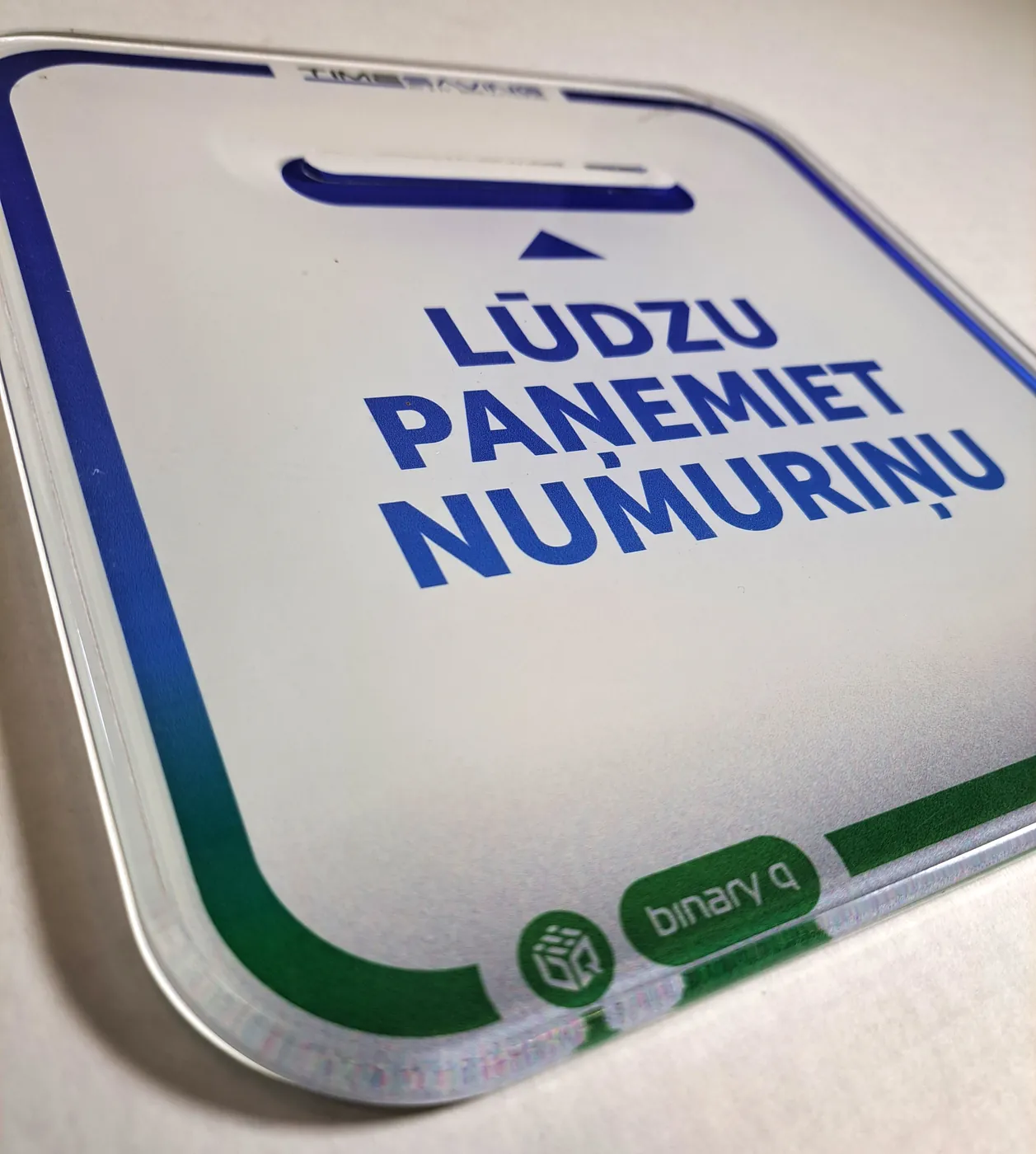Printed acrylic front for a queue-ticket dispenser, with Latvian text asking people to take a number