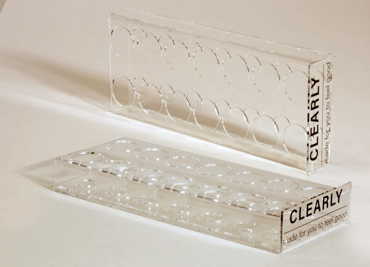 Two clear acrylic blocks with rows of round holes for small bottles, printed with a brand name