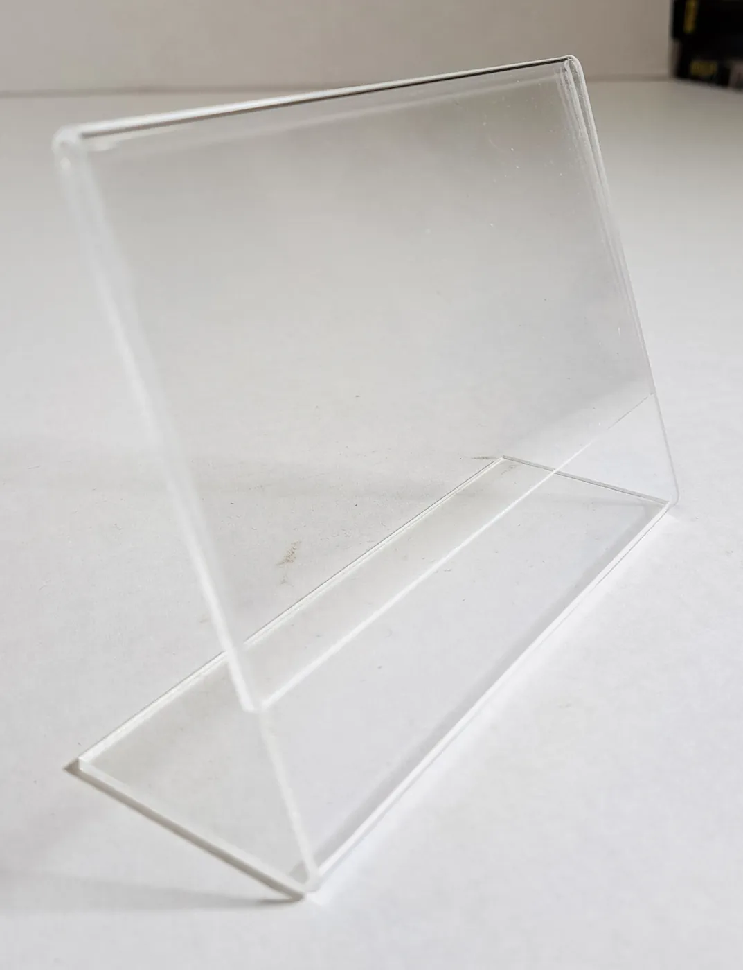 Clear L-shaped acrylic sign holder on a white surface