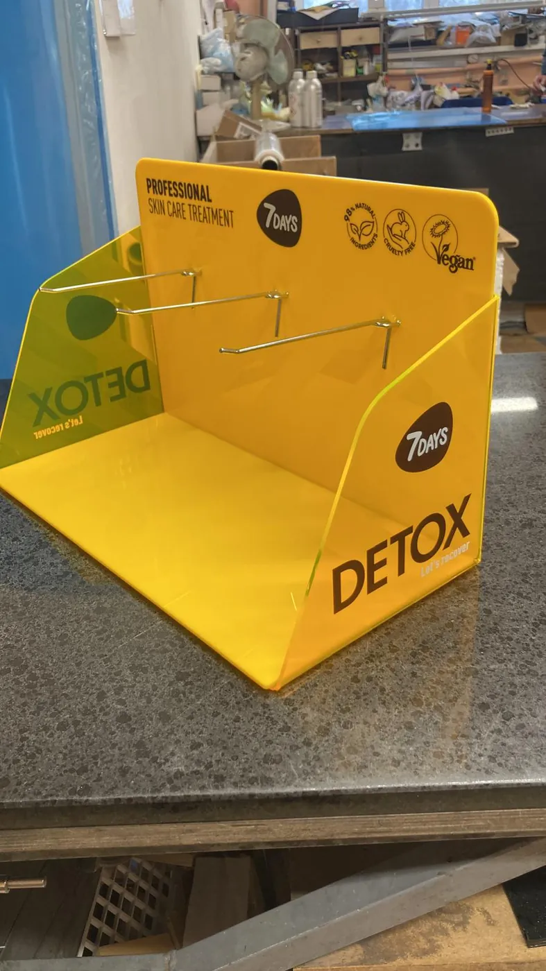 Yellow acrylic counter display with printed graphics and three metal hooks