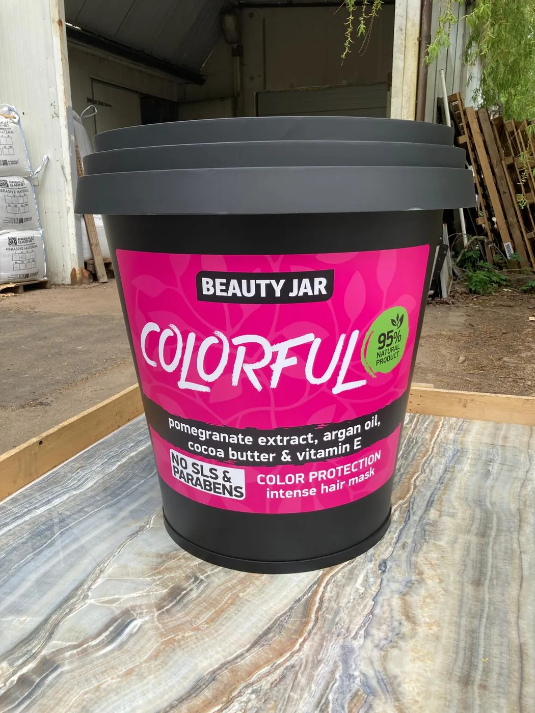 Cosmetics jar made as a display model, with a dark ribbed lid and a printed pink label, on a stone table outdoors