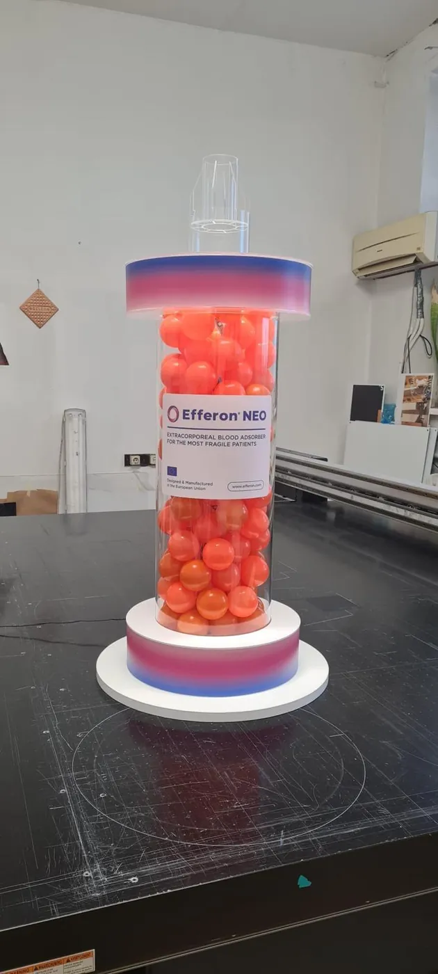 Clear column filled with orange balls between two coloured rings, on a round white base