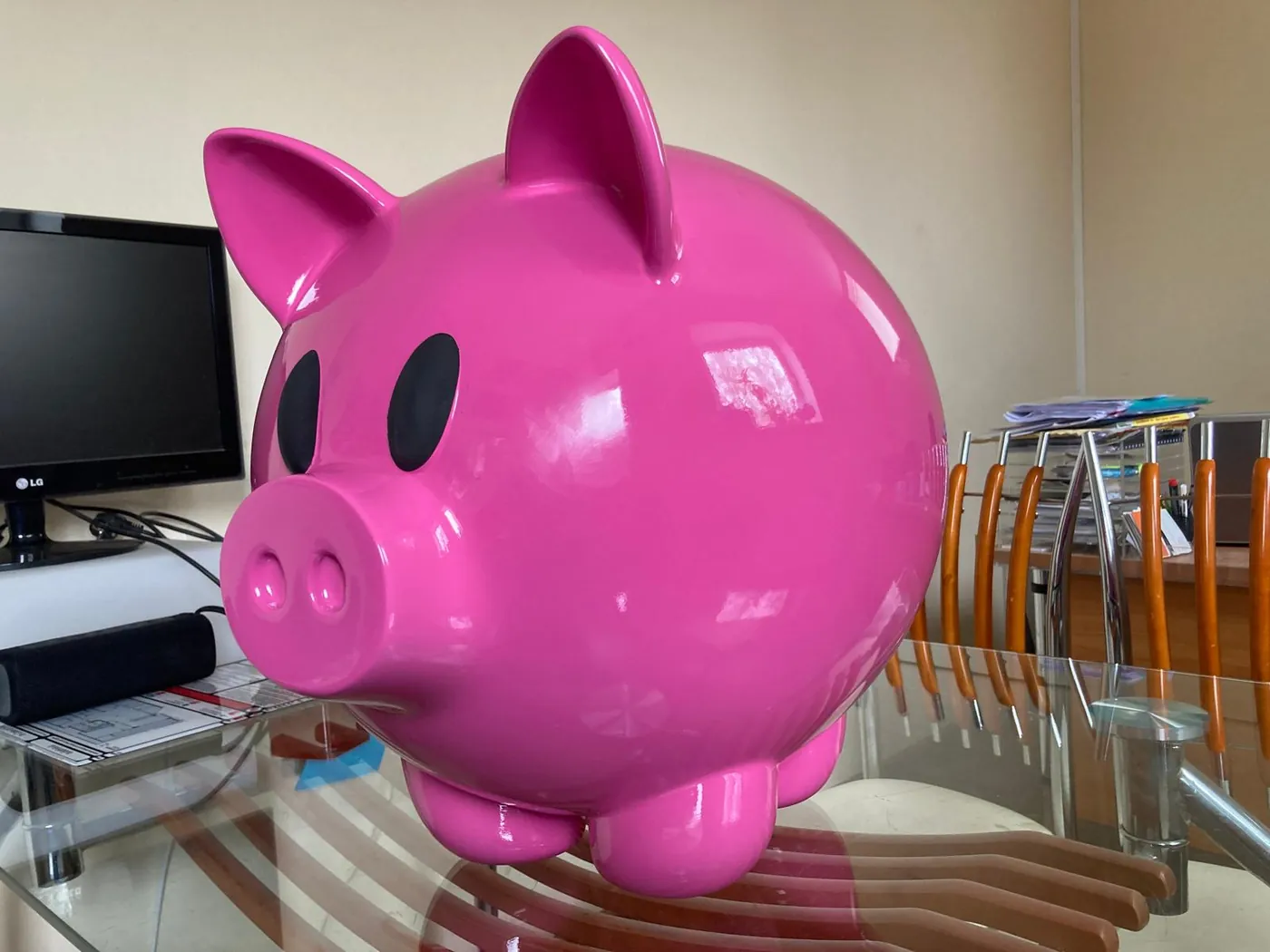 Large glossy pink pig figure with black eyes, standing on a glass table