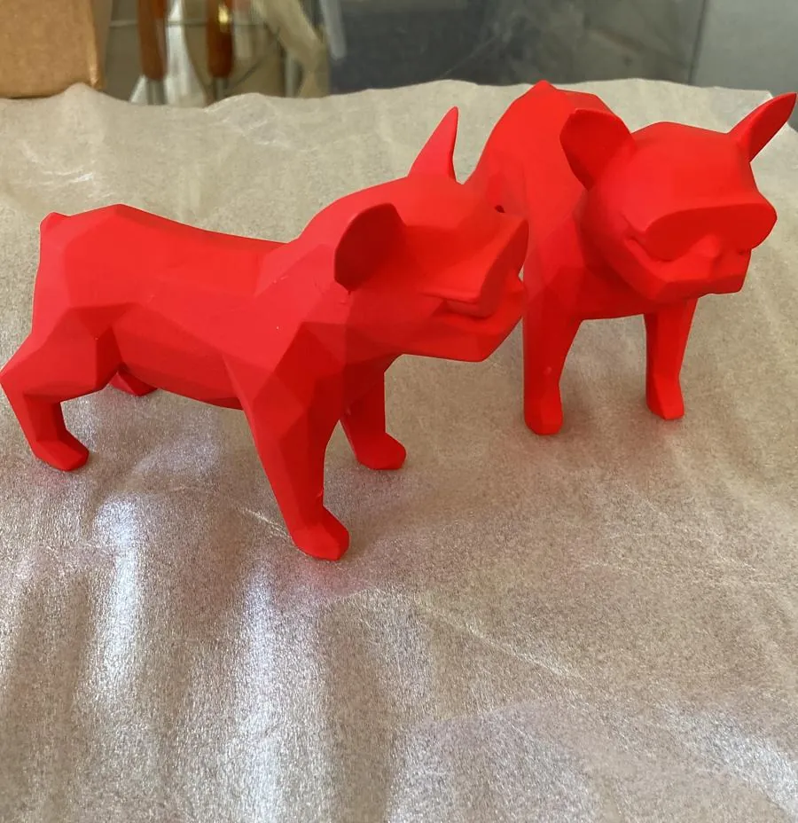 Two red faceted dog figures standing on a white cloth