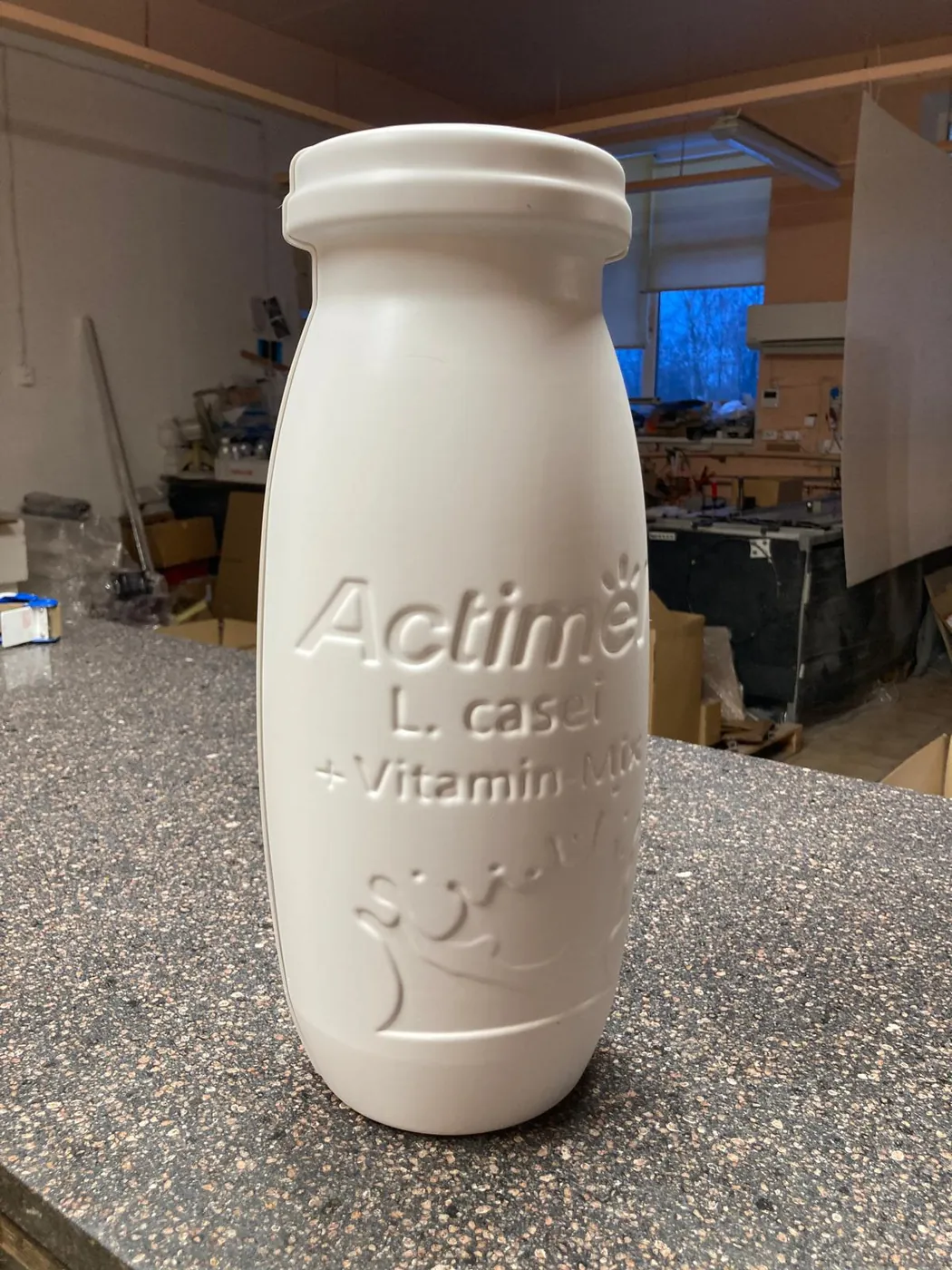 White bottle display model with embossed lettering and a splash motif, on a stone worktop in the workshop