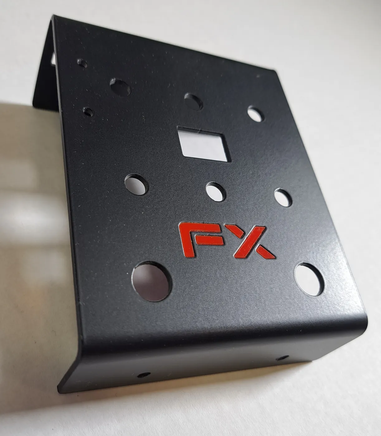 Bent black metal bracket with round and square cut-outs and a red logo inlay