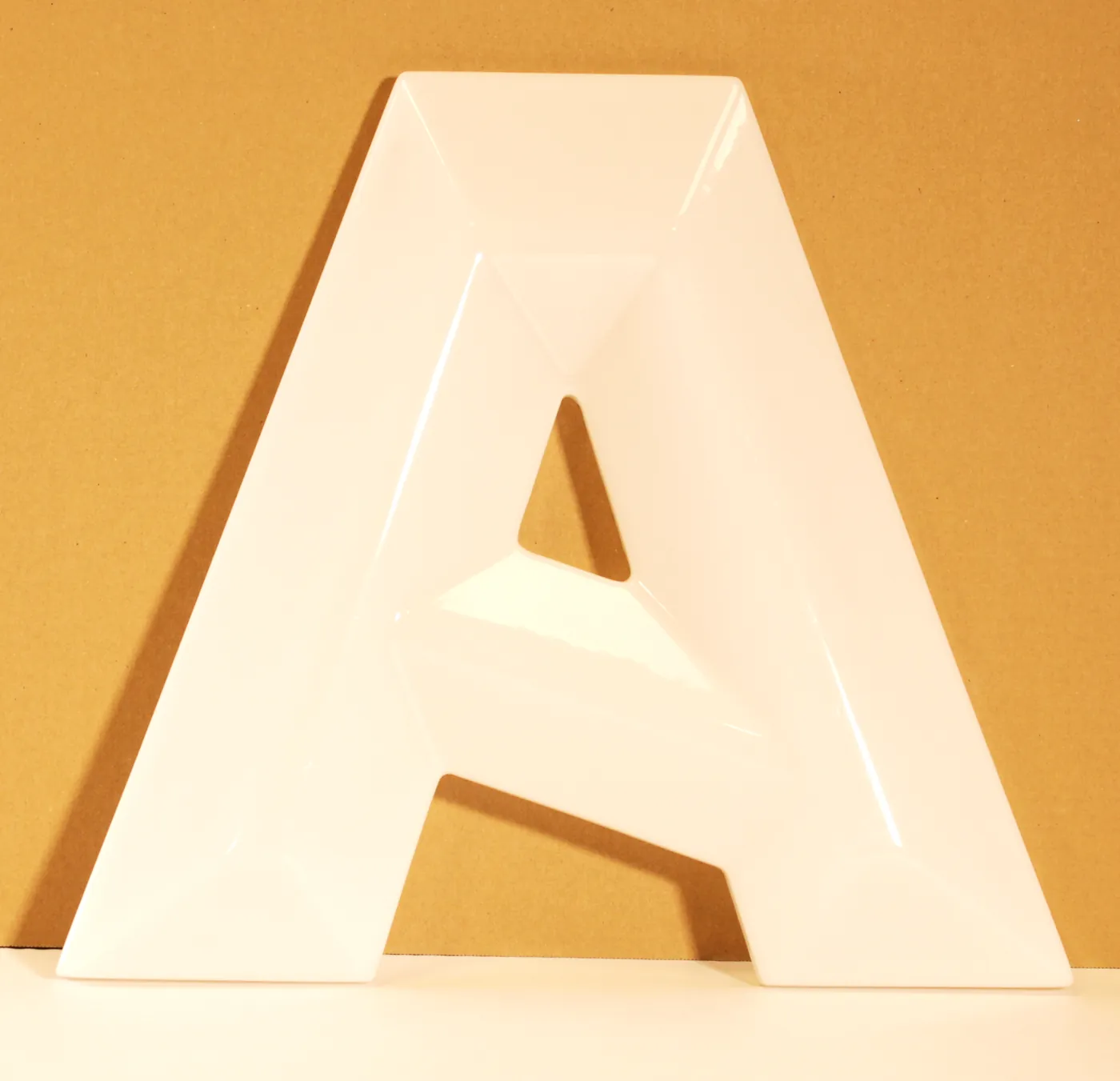 Glossy white letter A in plastic with bevelled faces, standing against an orange background