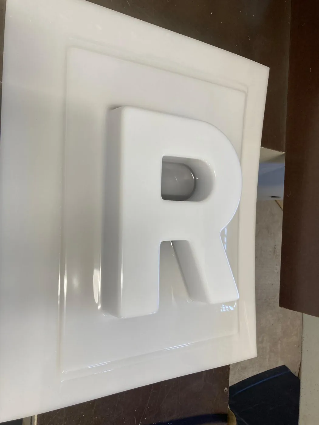 Glossy white letter R formed in plastic, still on its untrimmed sheet