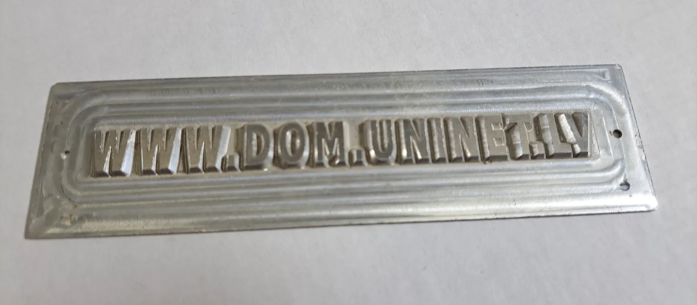 Metal plate with raised letters spelling a web address, inside a raised border