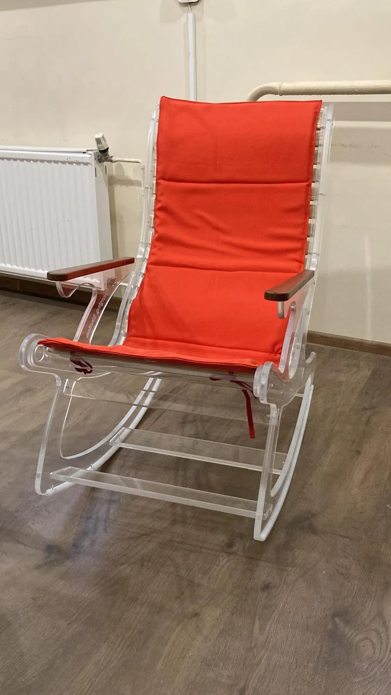 The same clear acrylic rocking chair seen from the front, with its orange cushion