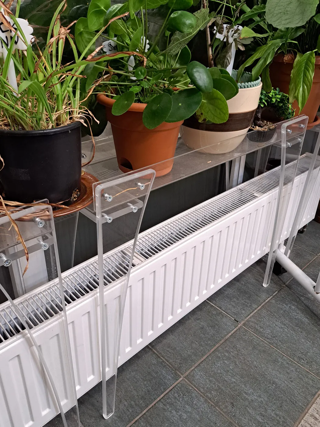 Clear acrylic plant stand over a radiator, holding potted plants