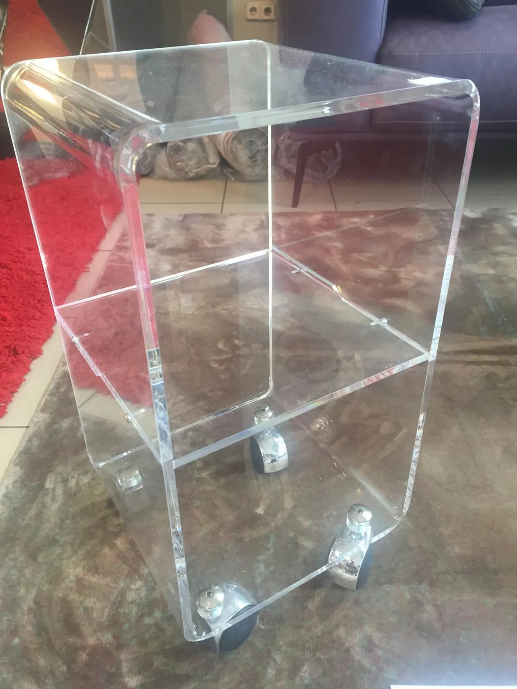 Clear acrylic side table with a lower shelf, standing on four castors