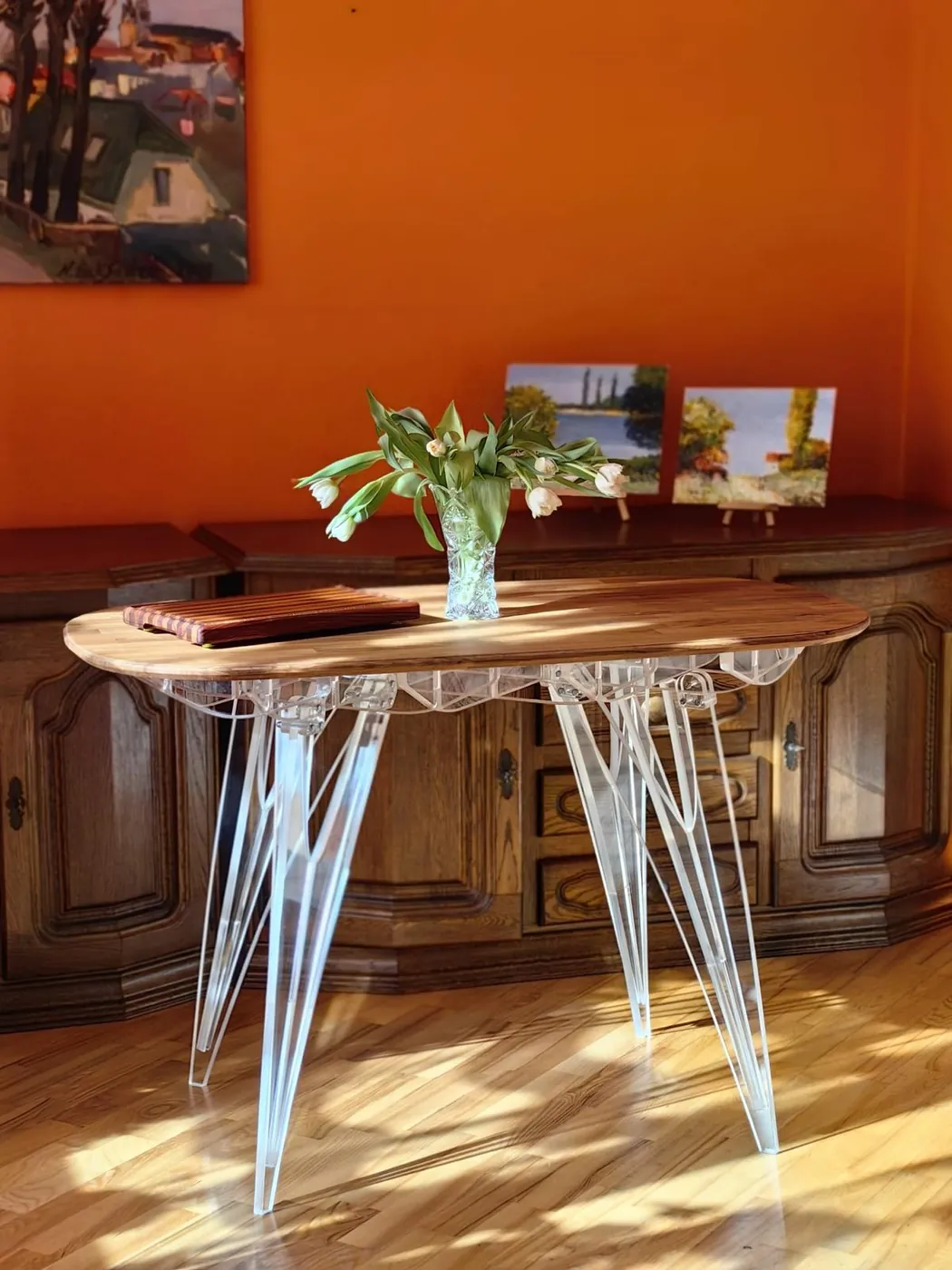 Small table with a dark wooden top on clear acrylic legs, in a sunlit room