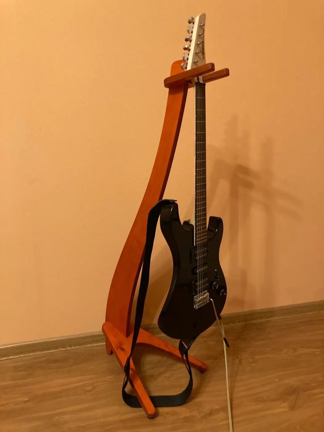 Curved wooden guitar stand holding an electric guitar against a wall