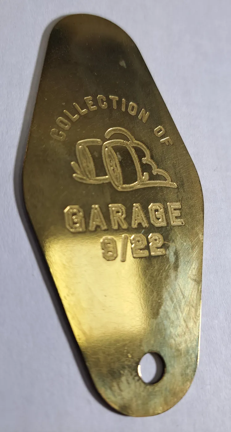 Gold-tone key tag with a garage design and lettering in relief