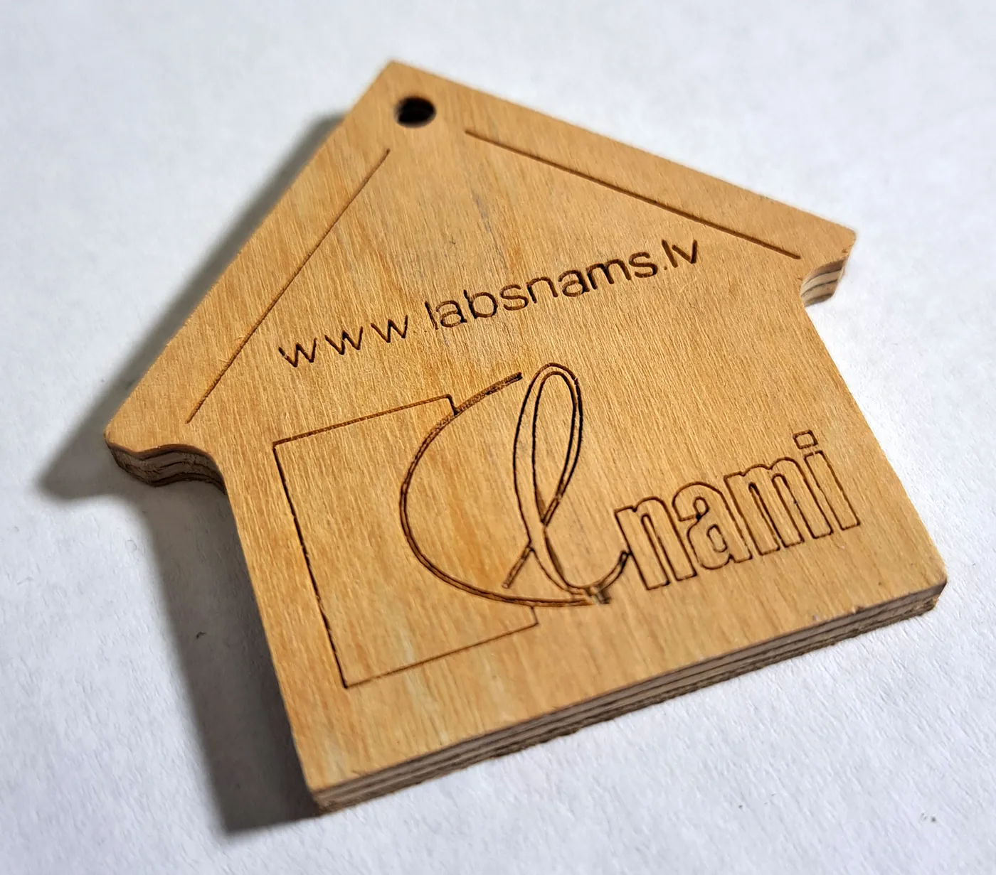 House-shaped plywood tag engraved with a logo and a web address