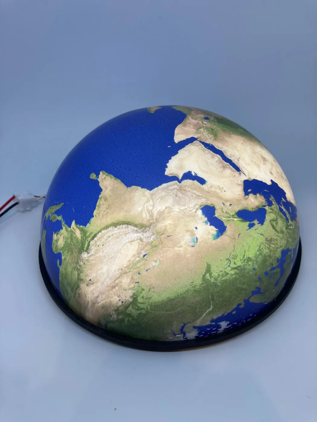 Earth model with blue oceans and green and sand-coloured land, on a black ring base