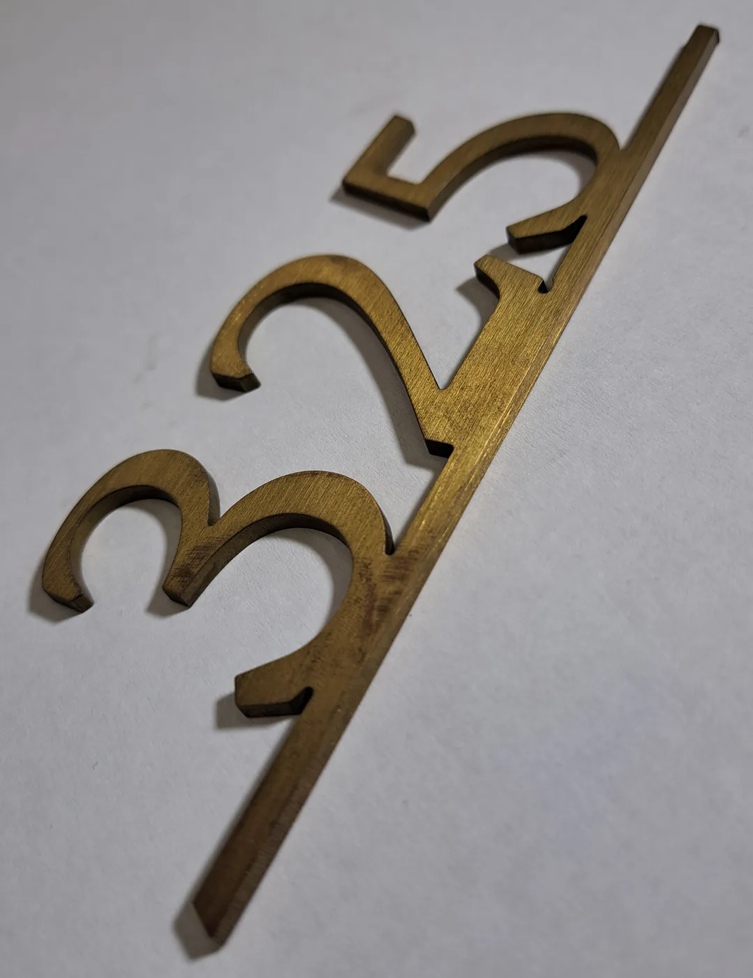 Gold-tone numerals 325 cut from metal sheet and joined along a diagonal bar