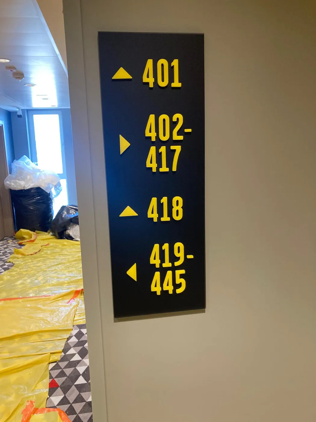 Black floor directory with yellow room ranges and arrows, on a pillar while the corridor is being fitted out