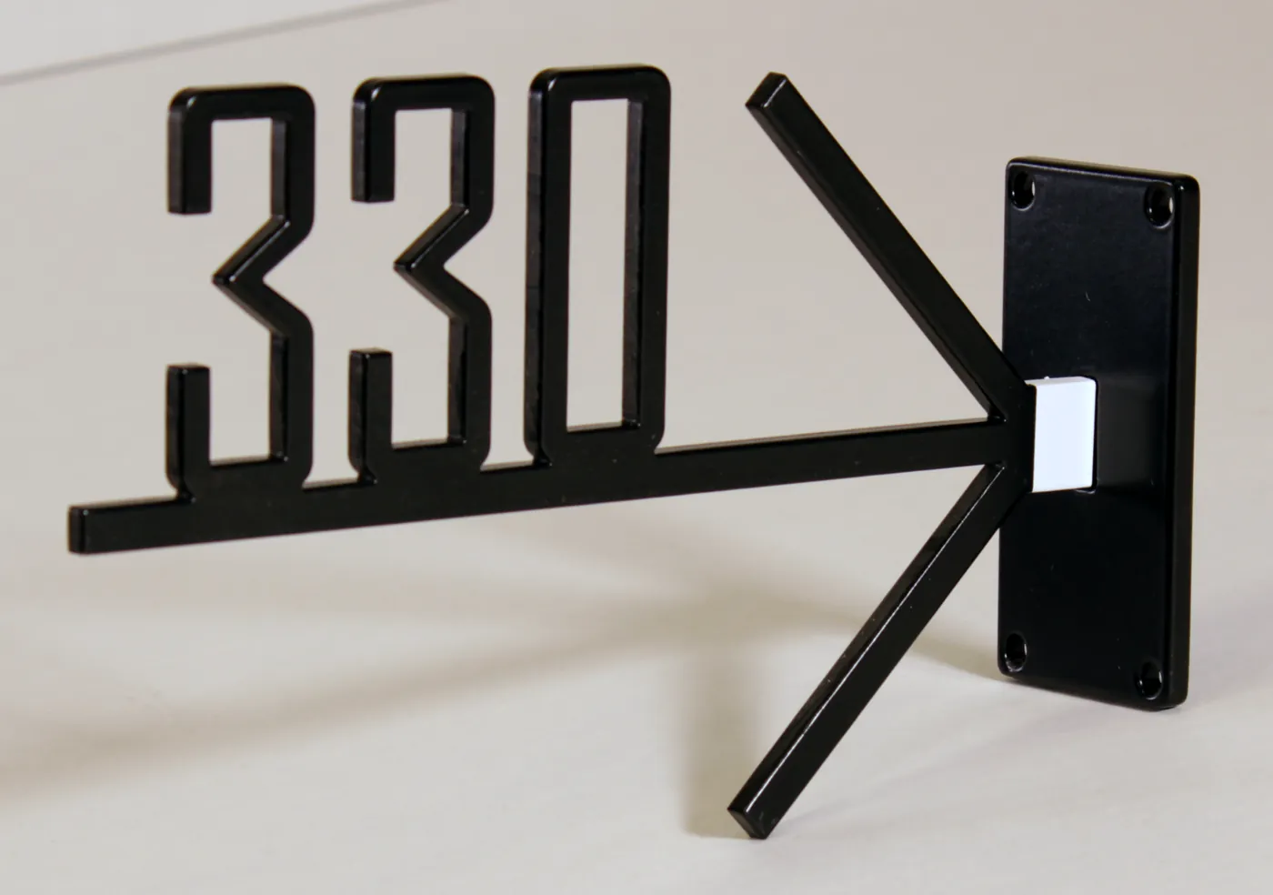 Black projecting sign with the number 330 and an arrow cut from one sheet, on a wall bracket