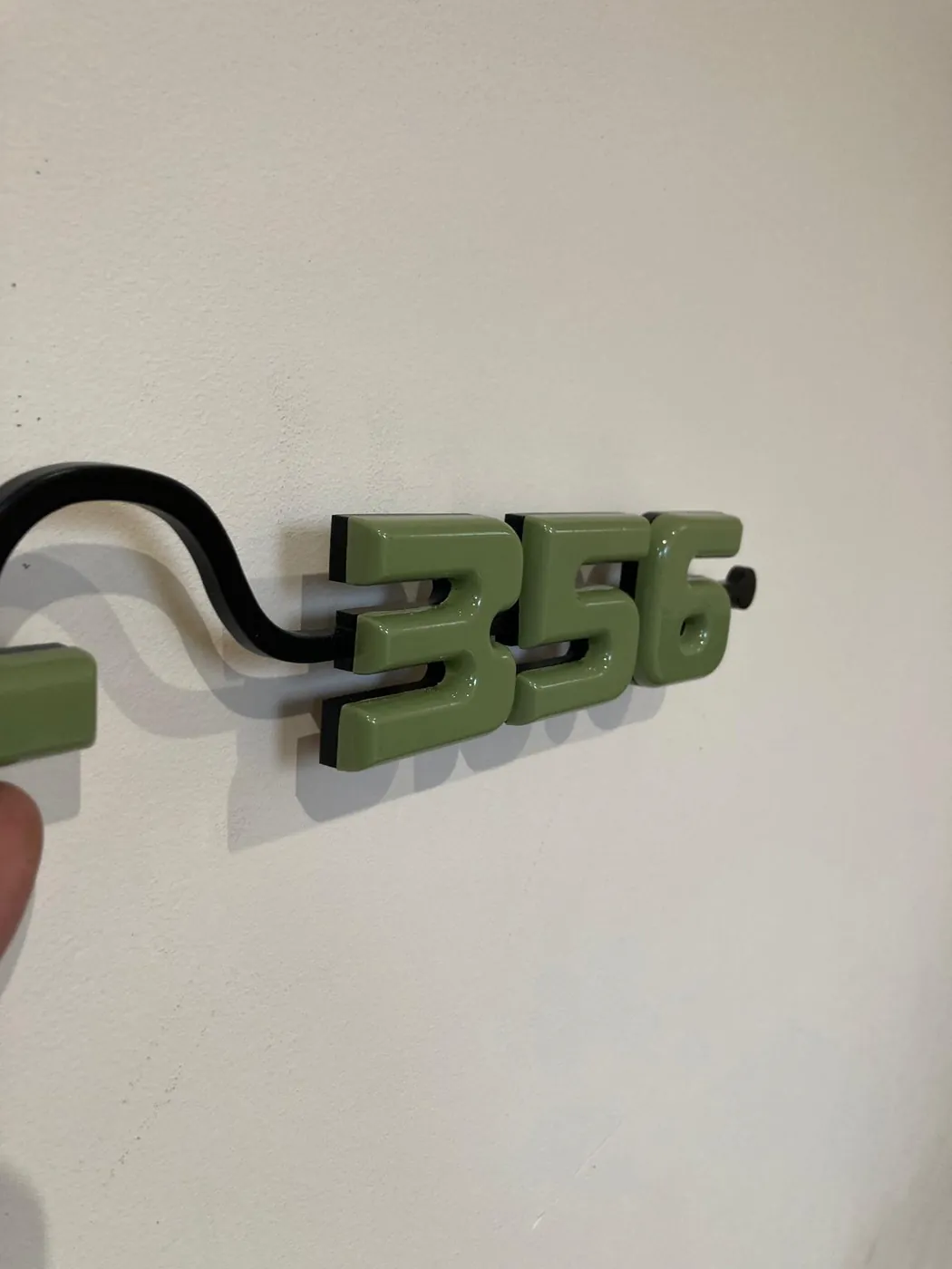 Green numerals 356 on a curved black bracket, held against a wall