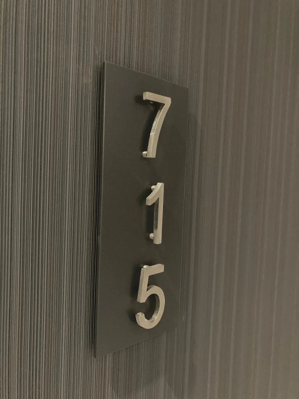 Tall dark plate with raised silver-grey numerals 715 on a textured corridor wall