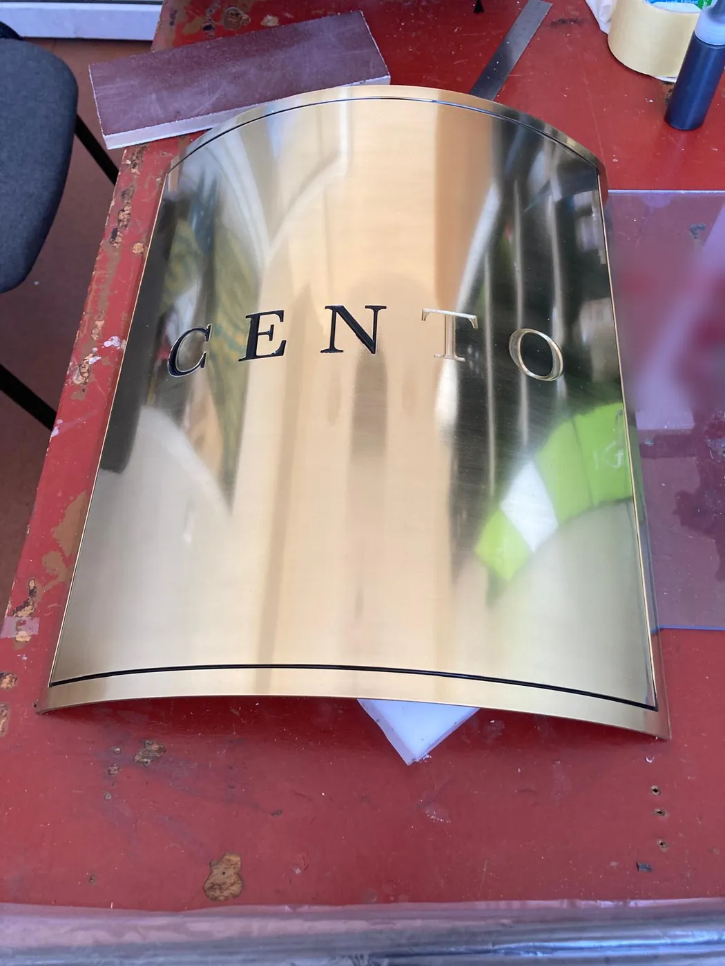 Curved mirror-finish metal plate with a name in dark capital letters, on the workbench