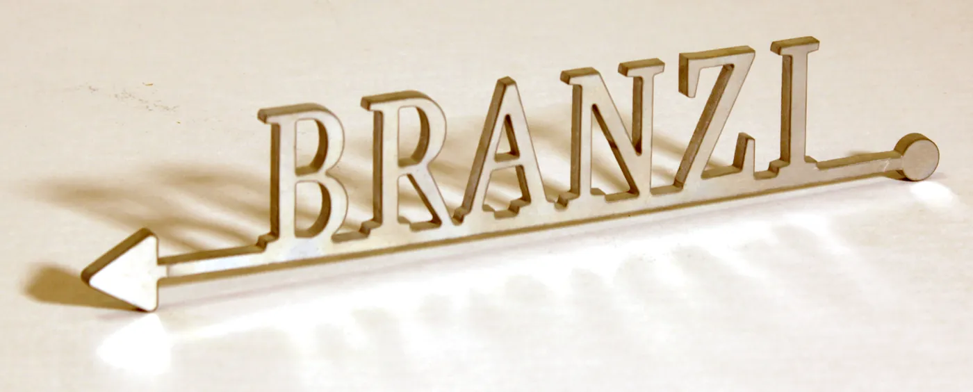 Gold-tone name cut out of metal and joined to an arrow, casting a shadow on a white wall