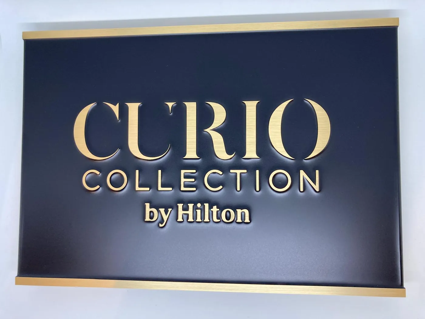 Hotel sign with raised gold-tone letters on a dark panel, framed by gold-tone strips at the top and bottom