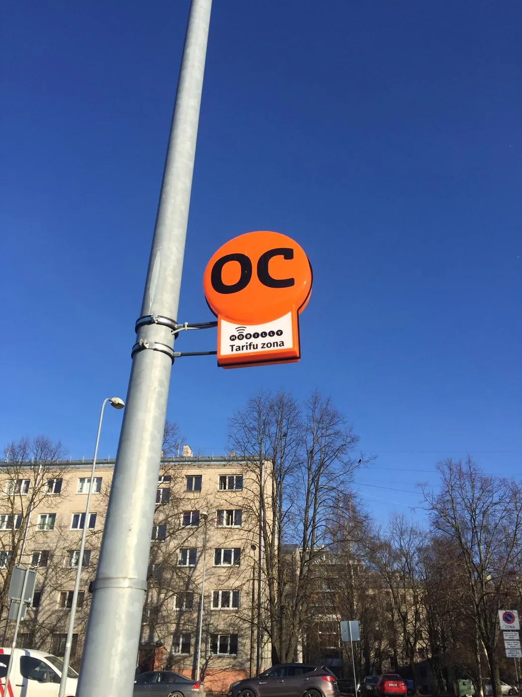 Round orange sign with a small panel below it, clamped to a street lamp pole