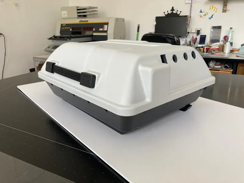 Two-part plastic enclosure with a white top, a dark base, a carry handle and round openings on the side