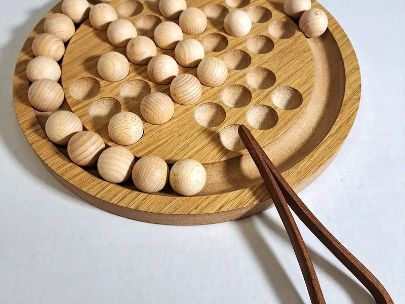 Round wooden solitaire board with a full set of wooden balls and a pair of wooden tongs