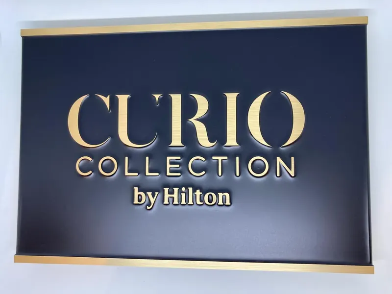 Hotel sign with raised gold-tone letters on a dark panel, framed by gold-tone strips at the top and bottom