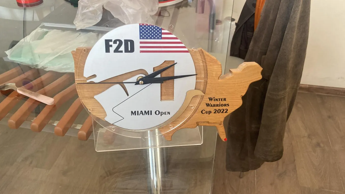 Wooden trophy shaped like a map, with a printed clock face, a flag and the event name, on a clear stand